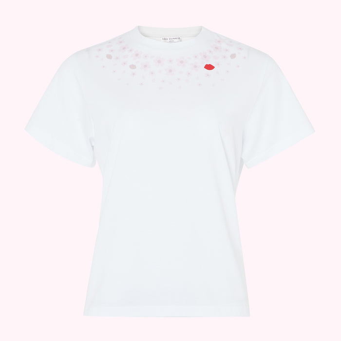 White short-sleeved t-shirt with pink cherry blossom and red lip print near neckline against pink background.