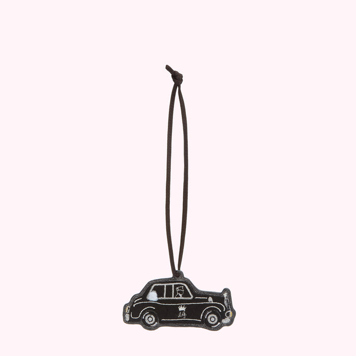 Black leather luggage tag shaped like a London cab, hanging from a brown cord.