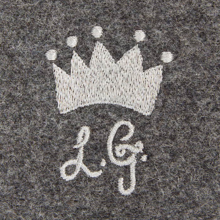 Close-up of grey felt fabric with embroidered silver crown and initials "L.G."