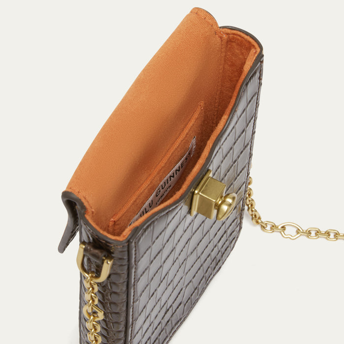 Close-up of a dark brown croc effect embossed leather bag with a gold clasp and chain strap, showing a orange interior lining.