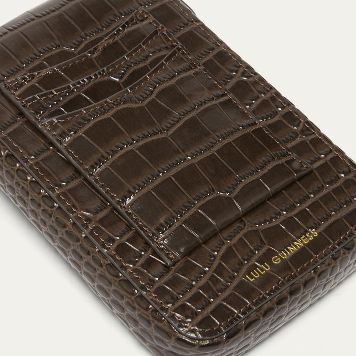 A close-up of a dark brown croc effect embossed leather bag, showing the textured pattern and gold 'LULU GUINNESS' branding, set against a clean off-white background.