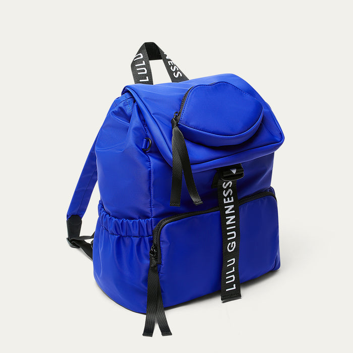 Cobalt blue backpack with black branded 'Lulu Guinness' straps on a light gray background