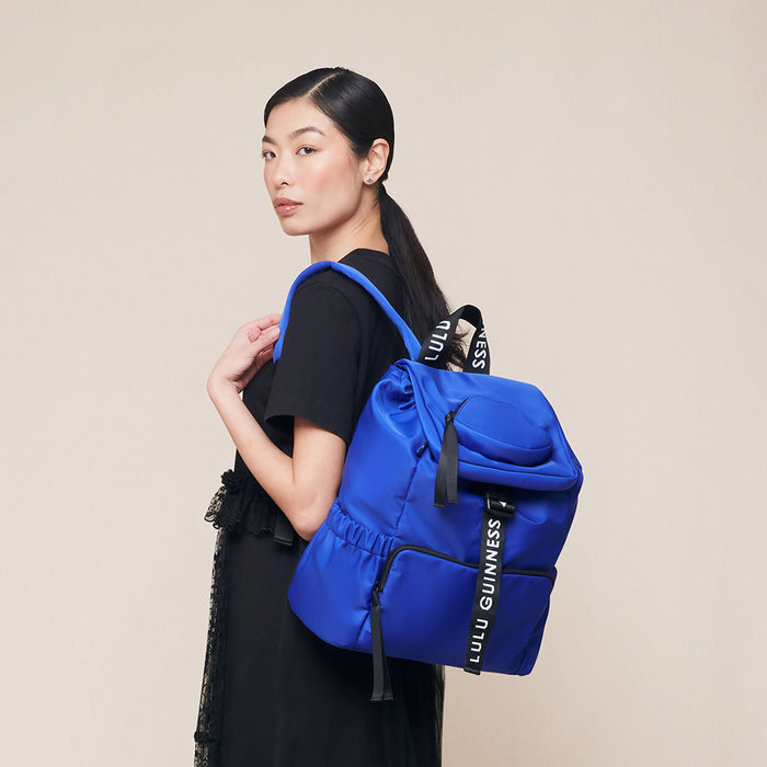 Woman carrying a blue backpack with 'Lulu Guinness' branding on a beige background