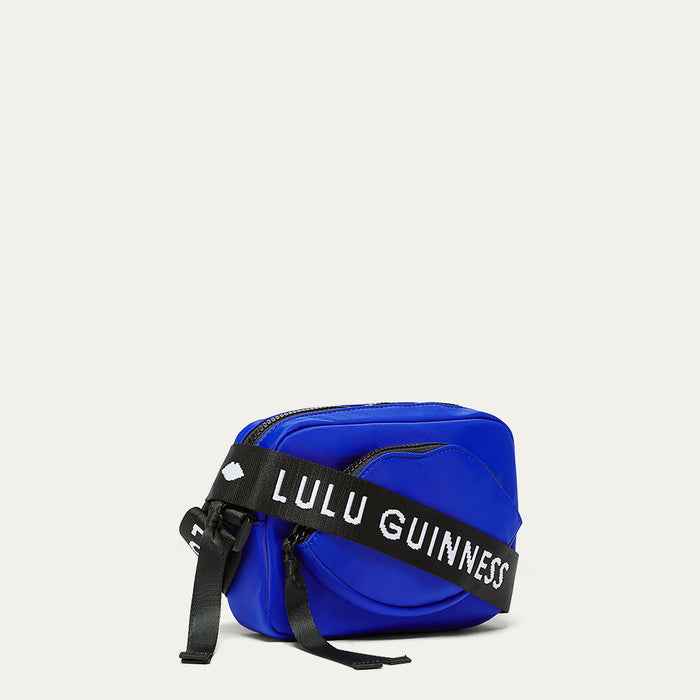 Cobalt blue crossbody bag with a black strap featuring 'Lulu Guinness' and lip shaped pocket on a light gray background