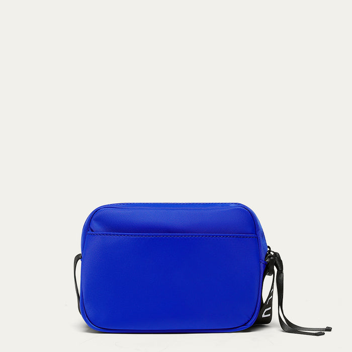 Image of the back of a cobalt blue  crossbody bag with a strap on a light gray background