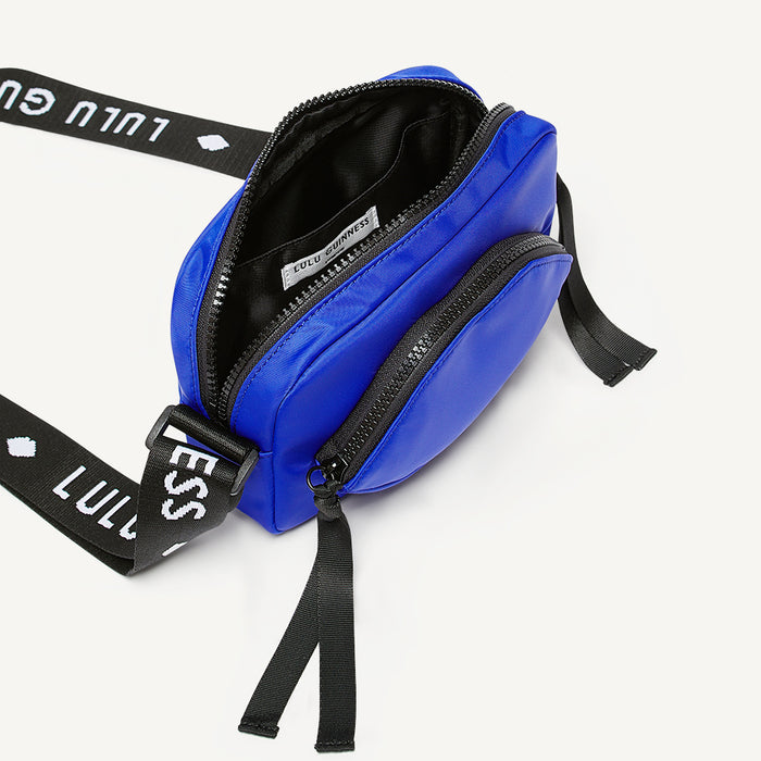 Cobalt blue crossbody bag open to reveal a black lining and inside pocket with a black 'Lulu Guinness' branded strap on a white background