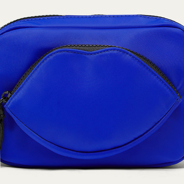 Close-up image of a cobalt blue crossbody bag with a black zipper and a lip shaped pocket on a white background