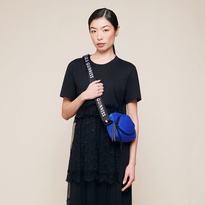 Woman wearing a black outfit with a blue bag featuring Lulu Guinness branding on a beige background