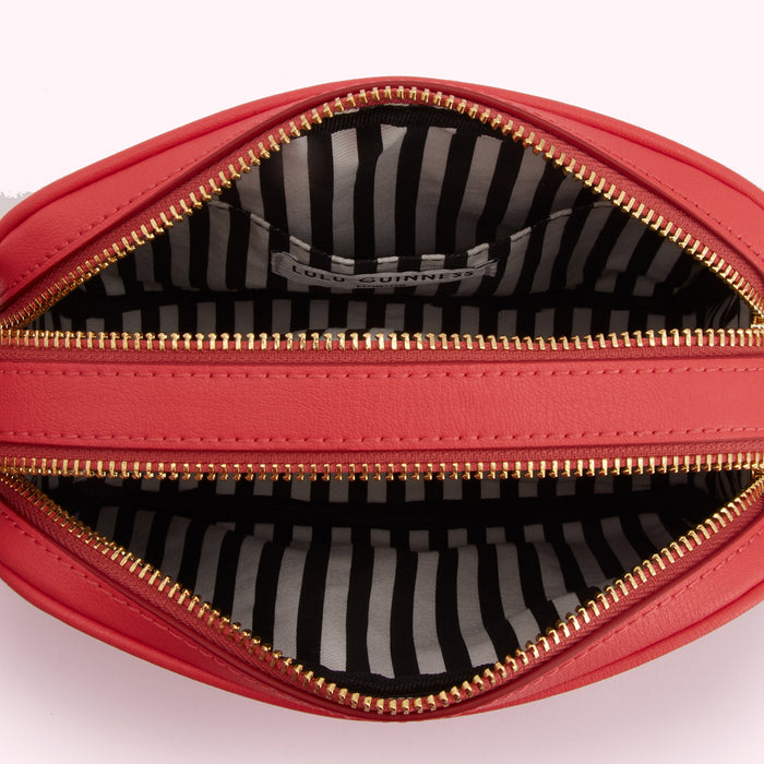 Inside of a coral Lulu Guinness crossbody bag, showing the black and white striped lining and gold zippers.