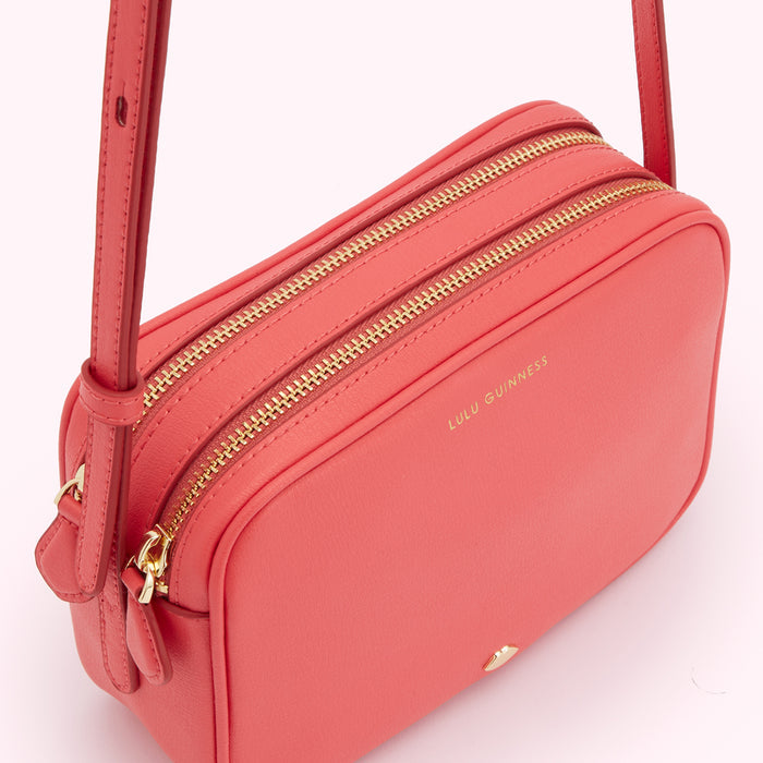 Coral Lulu Guinness crossbody bag with gold zippers.