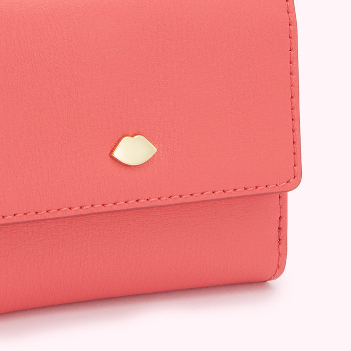 Close-up of a coral-coloured leather wallet with a gold lip-shaped emblem.