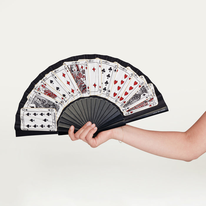 Person holding a handheld fan open with a deck of card design.