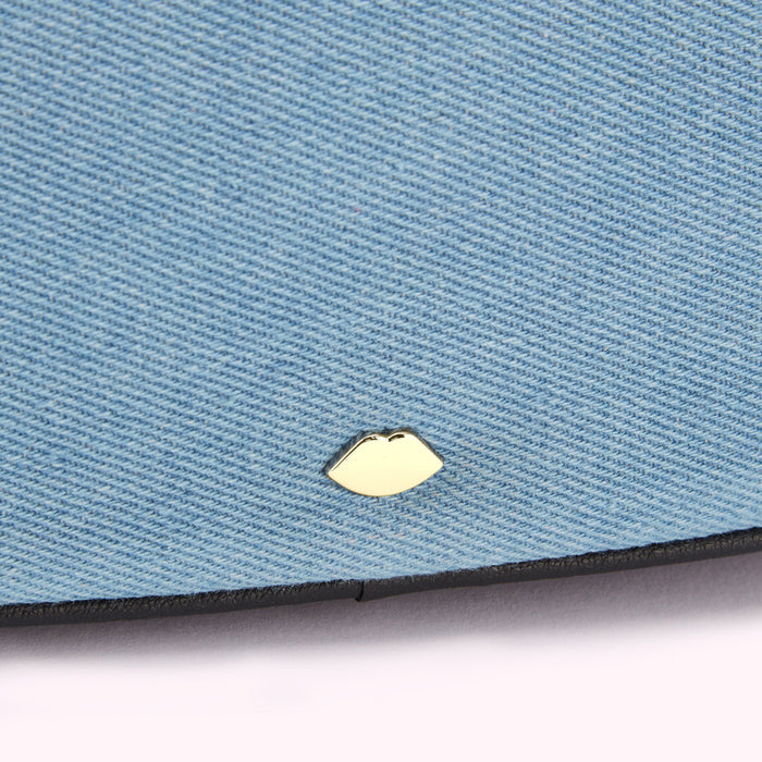 Close-up of a light blue denim fabric with a gold lip-shaped emblem.