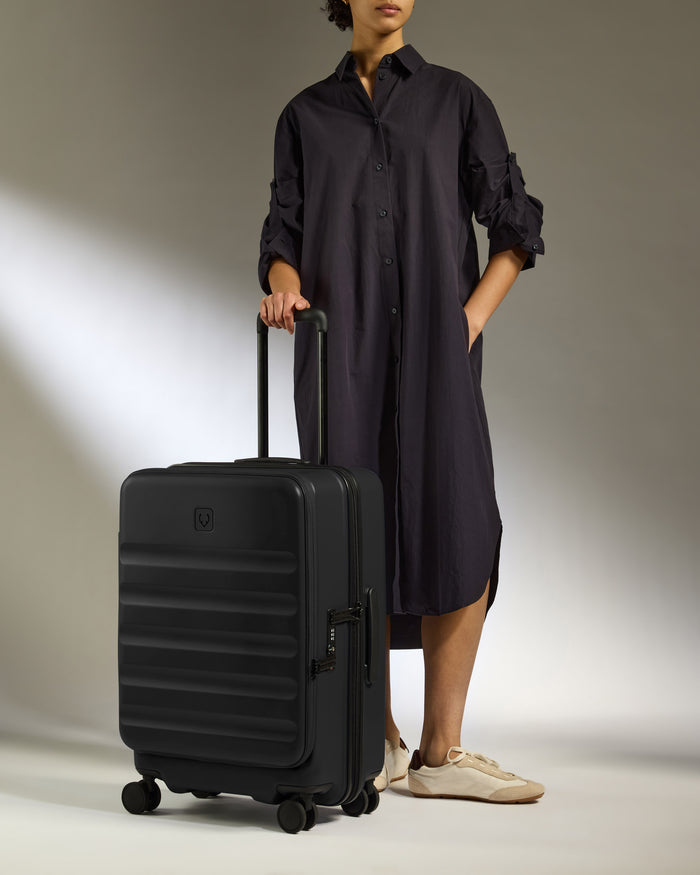 a woman in a long black dress and white sneakers holding a suitcase