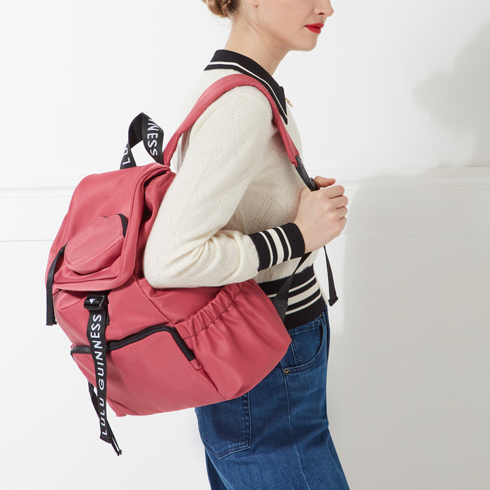 Woman wearing a blush pink Lulu Guinness backpack against a white background.