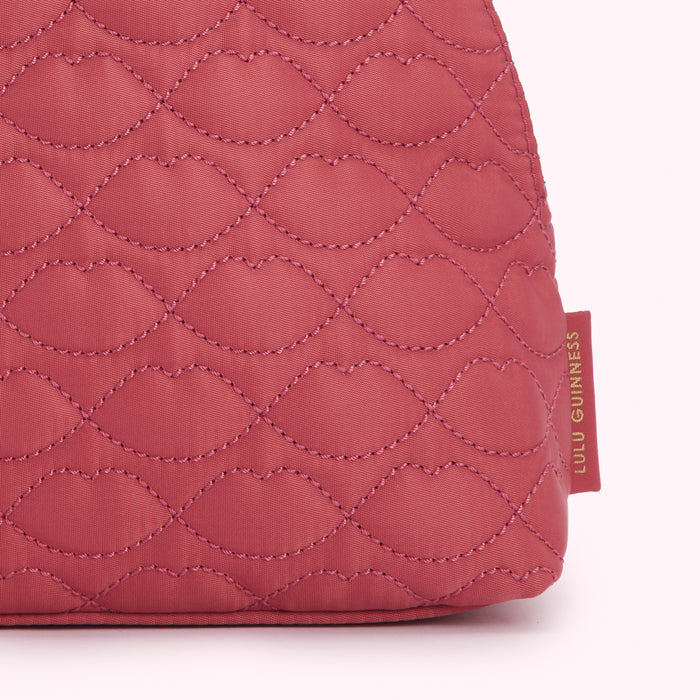 Close-up of a dusty rose quilted Lulu Guinness bag with a lip pattern.