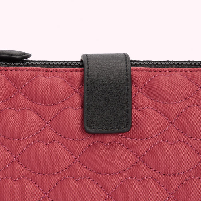 Close-up of a quilted red purse with a black leather strap.