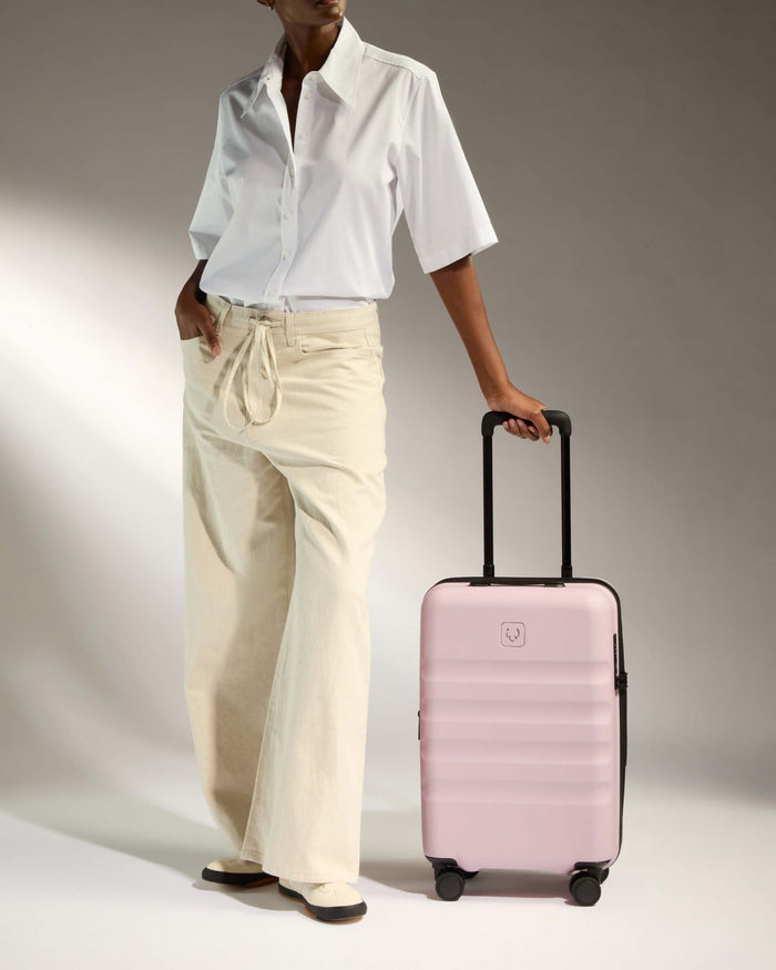 a woman in white shirt and beige pants holding a pink suitcase