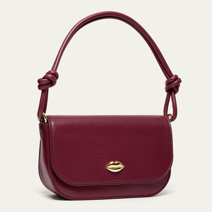 Burgundy leather shoulder bag with a gold lip feature and a knotted shoulder strap on a light grey background