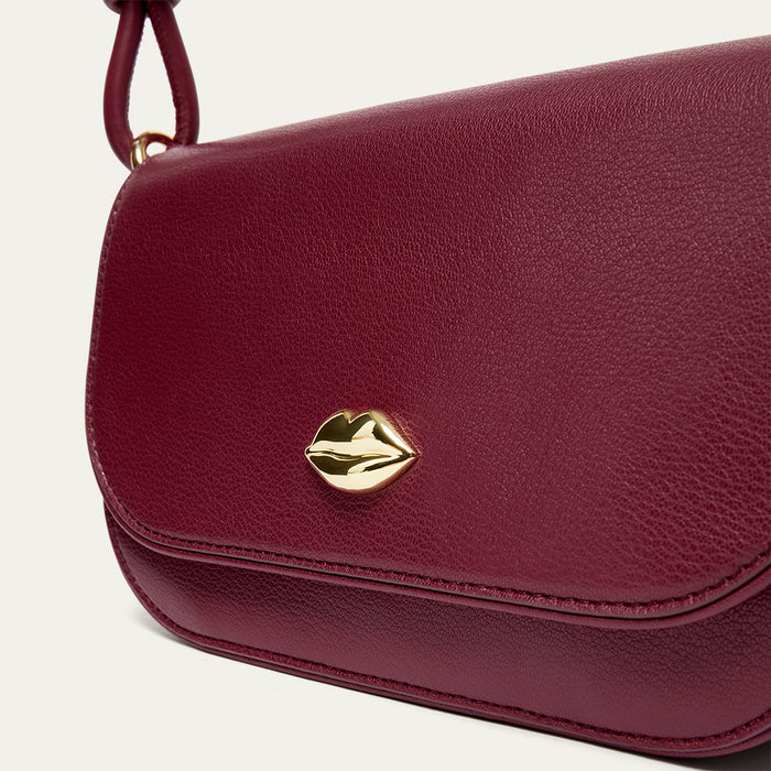 Close-up of the gold lip detail on a burgundy leather shoulder bag.