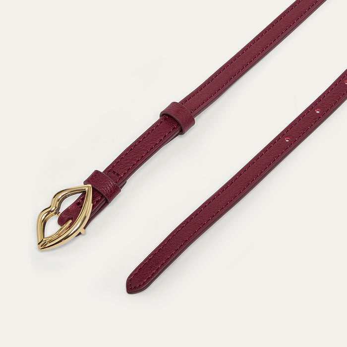Burgundy leather belt with a gold lip-shaped buckle on a light grey background