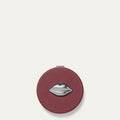 Round burgundy red compact mirror with a silver lip design on a light beige background
