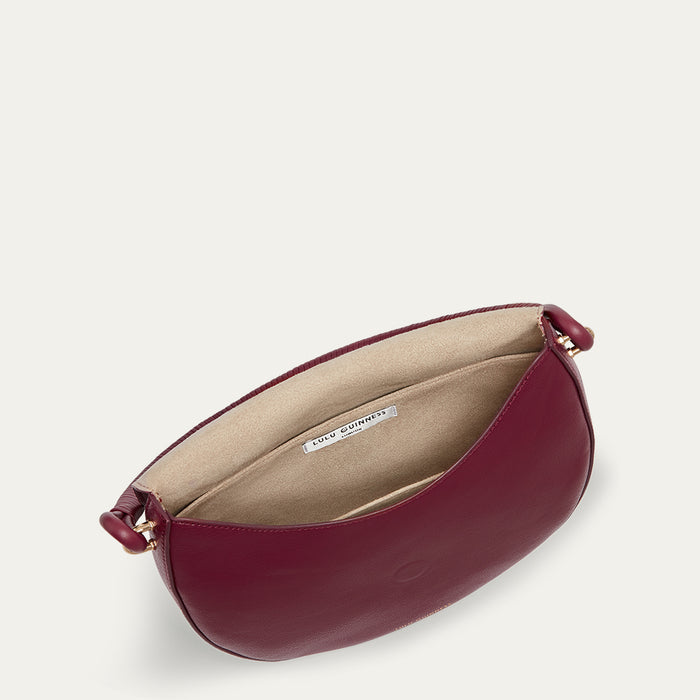 Inside image of a burgundy leather handbag with a beige interior on a light grey background
