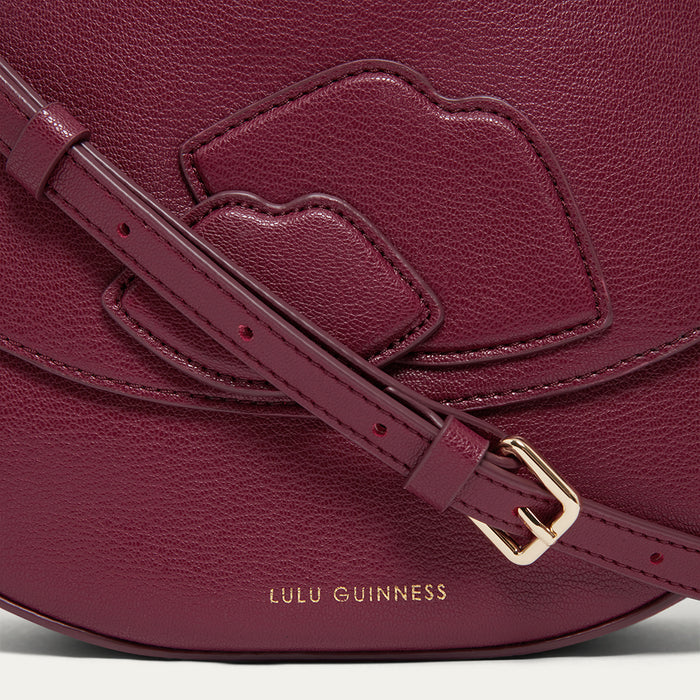 Close-up the lip detail and gold buckle of a burgundy leather handbag with gold printed ' Lulu Guinness' branding.