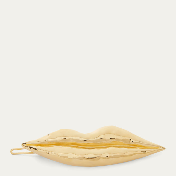 A gold metallic lips-shaped hair  clip with a textured, hammered finish, shown against a solid off-white background.