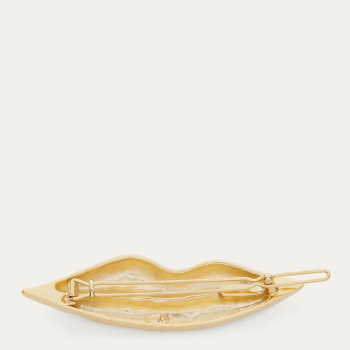 A gold-tone metal hair pin shaped like lips, shown from the back on a clean, solid off-white background.
