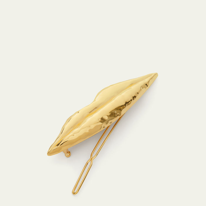 A gold metallic hair clip shaped like stylized lips, shown on a clean off-white background.