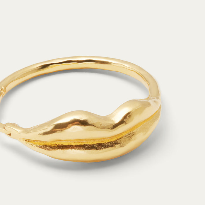 Close-up of a textured gold hoop earring with a organic lip-like design, photographed on a clean off-white background.