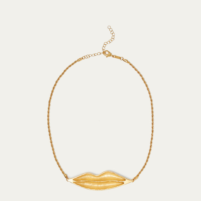 A gold chain necklace featuring a sculptural, textured gold lips pendant, displayed against a solid off-white background.