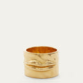 A wide gold ring featuring a sculpted, textured lips motif on the front, photographed against a clean, light off-white background.