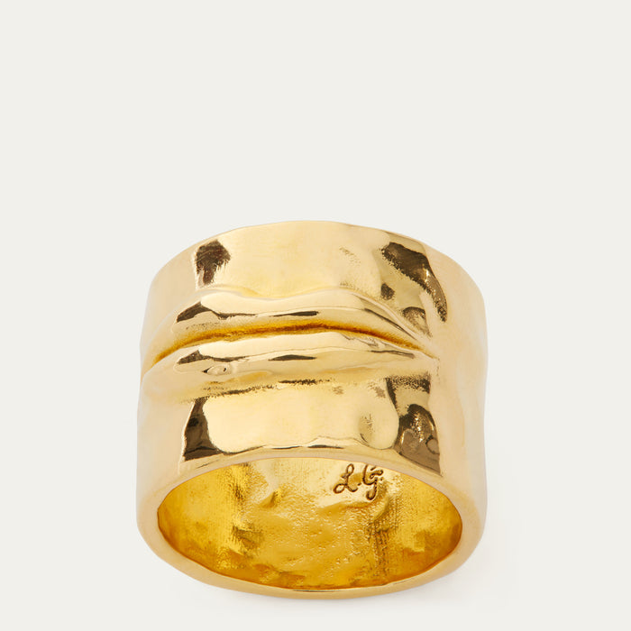 A wide, chunky gold ring with a textured, organic wavy surface and a hammered finish inside, photographed on a clean off-white background.
