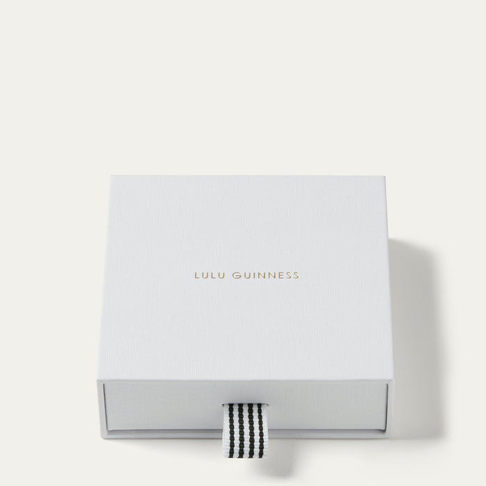 A square white Lulu Guinness gift box with a small black-and-white striped ribbon pull tab, photographed on a clean off-white background.