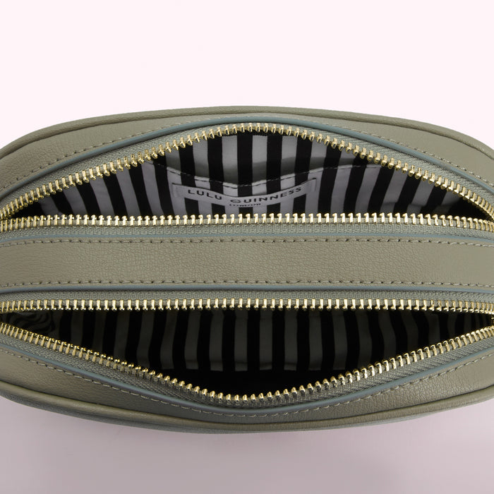 Interior of a sage green Lulu Guinness crossbody bag with gold zippers and black and white striped lining.