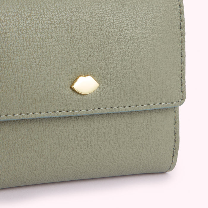 Close-up of a sage green leather wallet with a gold lip-shaped emblem.