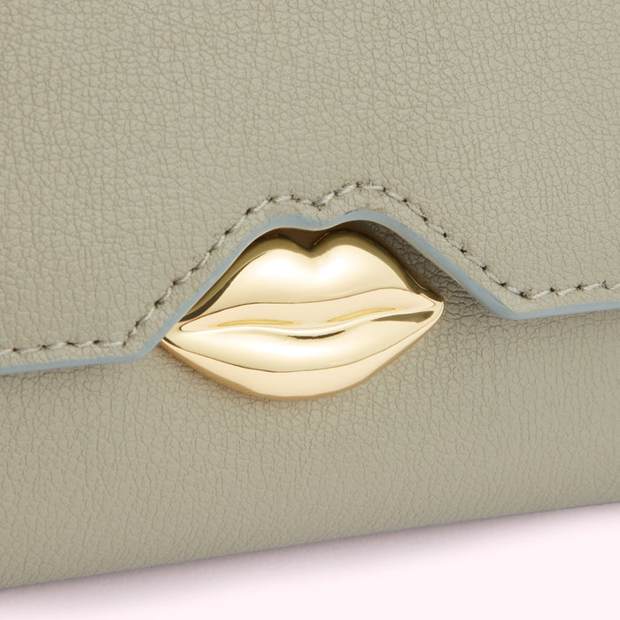 Close-up of a sage green leather wallet with a gold lip-shaped clasp.