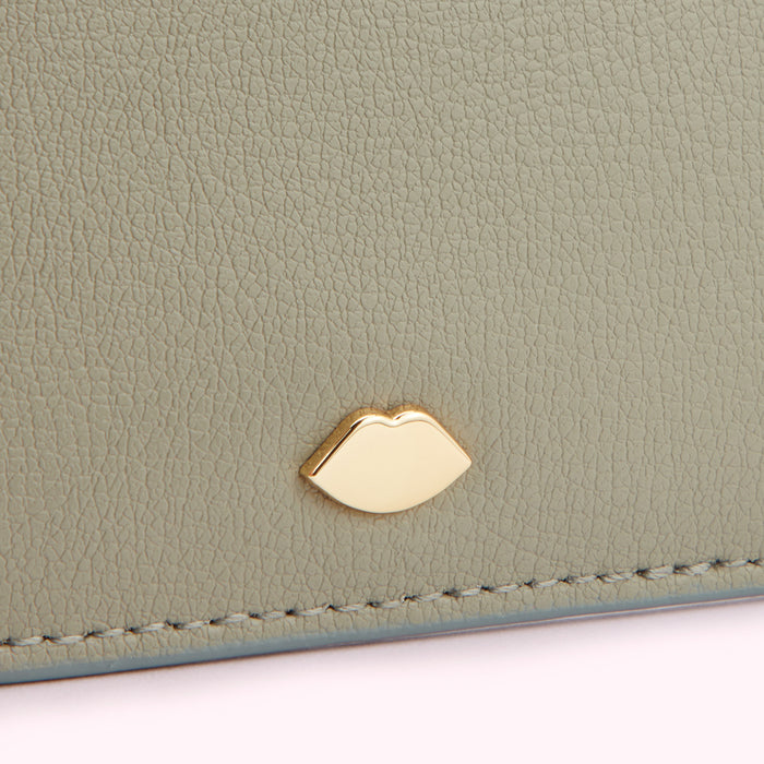 Close-up of a sage green leather wallet with a gold lip-shaped accent.
