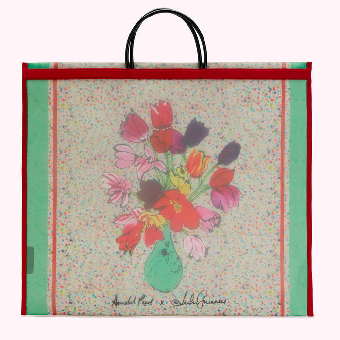 Large red and green tote bag featuring a whimsical illustration of tulips in a vase by Annabel Pearl in collaboration with Lulu Guinness, on an off-white background with multicolored confetti.