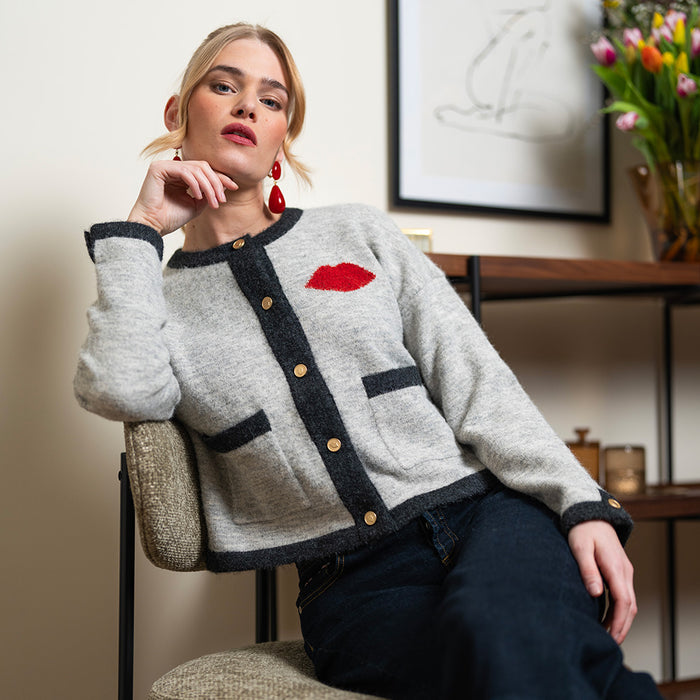 A women wearing a gray cardigan with black trim and red knitted lip detail.
