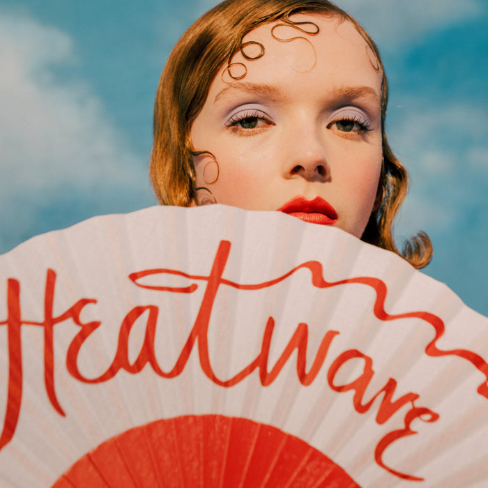 Person holding a 'Heatwave' fan with a blue sky background