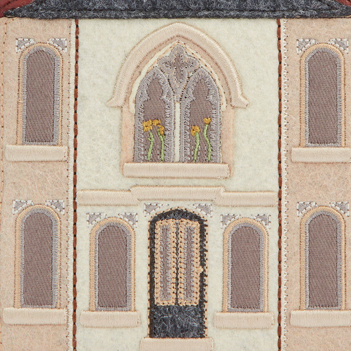 Close-up of a beige needlepoint depiction of a building facade with arched windows and a double door.