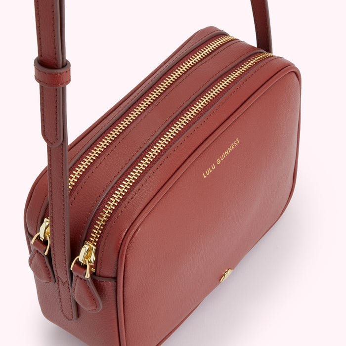 Close-up of a Lulu Guinness burnt-orange leather crossbody bag with gold zippers.