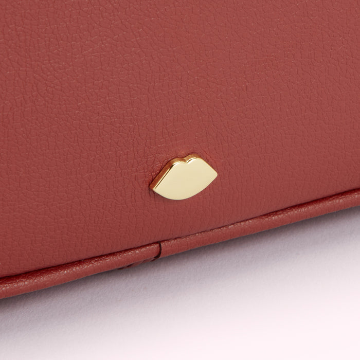 Close-up of a terracotta-coloured leather purse with a gold lip-shaped emblem.