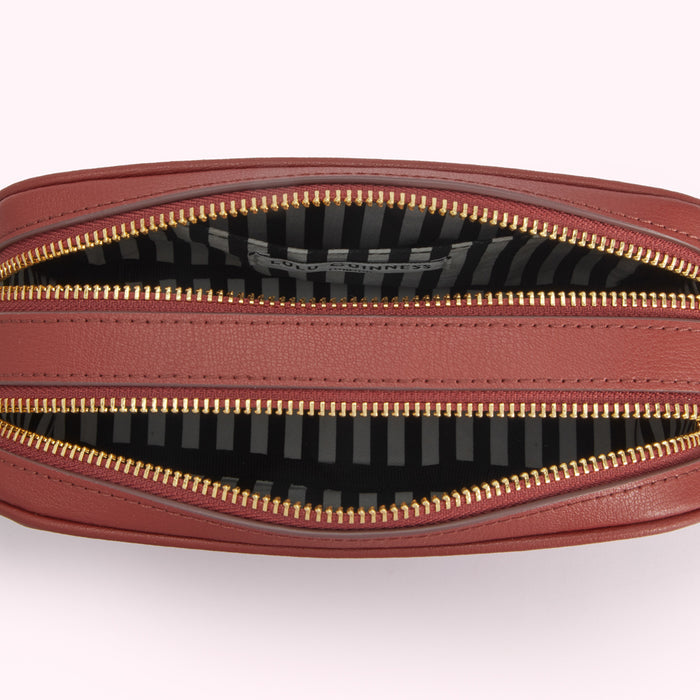 Interior of a red Lulu Guinness handbag with gold zippers and a black and white striped lining.