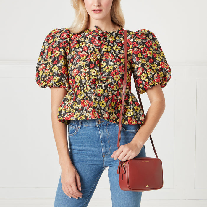 Woman in floral top and jeans holding a red crossbody bag.