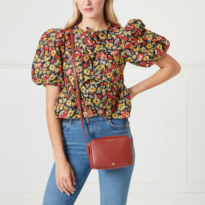 Woman in floral top and jeans wearing a red crossbody bag.