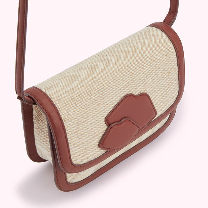 Beige canvas crossbody bag with brown leather trim and lip-shaped detail.